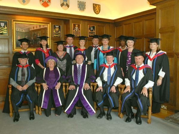IAM graduates and officers in academic dress posing beneath heraldic shields